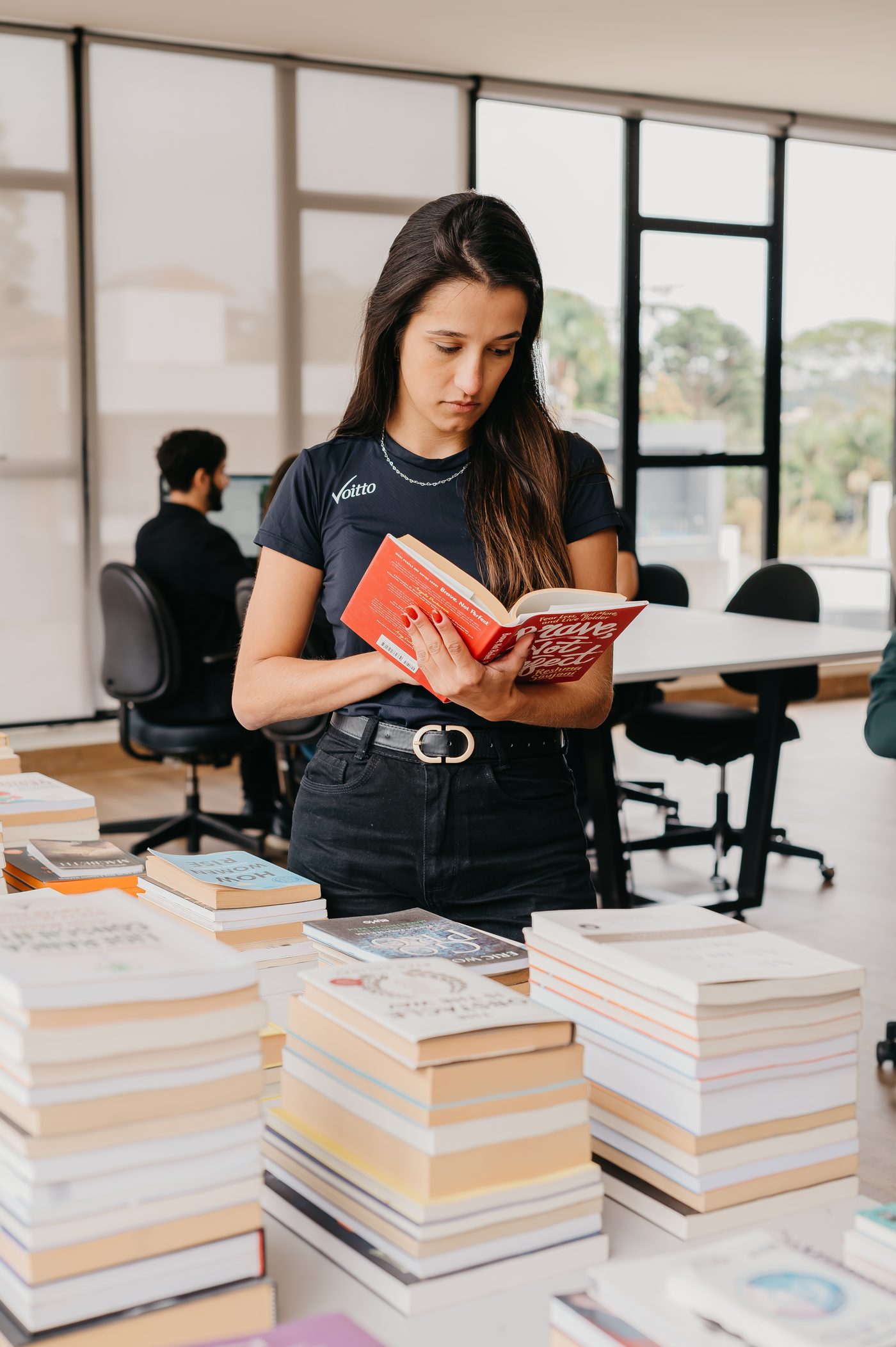 Colaboradora da Voitto lendo em pé, ao lado das pilhas de livros da sede